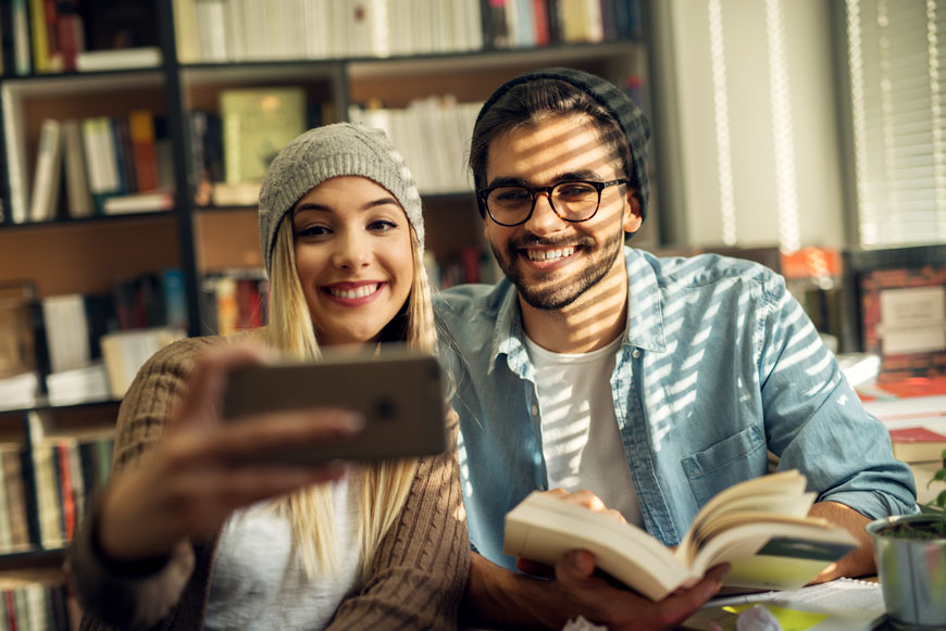 Close up of adorable cute stylish high school student couple taking a selfie in the library while learning together.