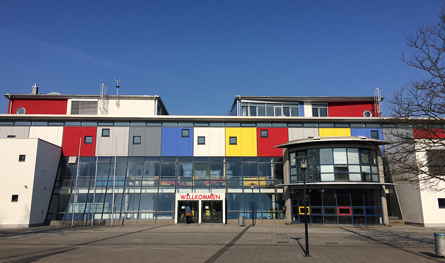 Mit einem Bauvolumen von über 10 Millionen Euro entstand 1993-1995 der ungewöhnliche und farbenfrohe Schulneubau des Gymnasiums Sanitz mit vielen offenen Begegnungsbereichen und verschiedene geometrische Baukörper und Materialien kombinierend.