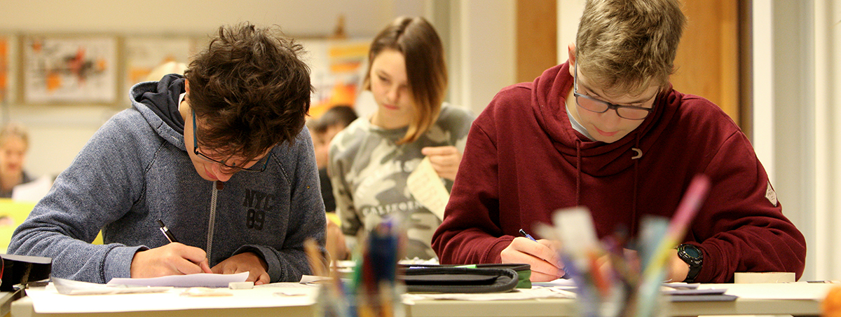 Zei Schüler sitzen am Tisch und schreiben in ihre Hefte, Foto: Silke Winkler (am Erasmus-Gymnasium Rostock)