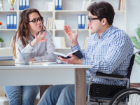 Beispielfoto: Eine Frau erklärt einem Mann im Rollstuhl etwas in einem Büro