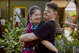 Ein junges Mädchen und ein junger Mann mit Trisomie 21 umarmen sich und lachen