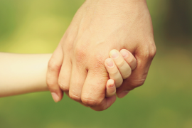 Hand eines Erwachsenen hält Händchen mit einer Kinderhand vor grünem Hintergrund