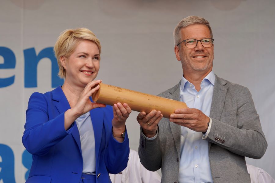 Die Ministerpräsidentin bei der Übergabe des Staffelstabes für den MV-Tag 2025 an Greifswalds Oberbürgermeister Dr. Stefan Fassbinder. Beide halten gemeinsam den Staffelstab fest.