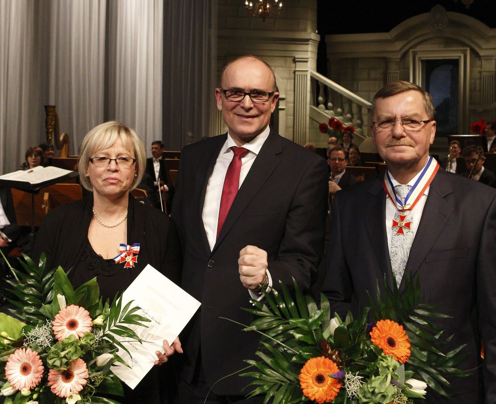 Der damalige Ministerpräsident Erwin Sellering mit den Ausgezeichneten Gudrun Schoeder und Wolfgang Remer, beide mit Blumensträußen und Urkunden