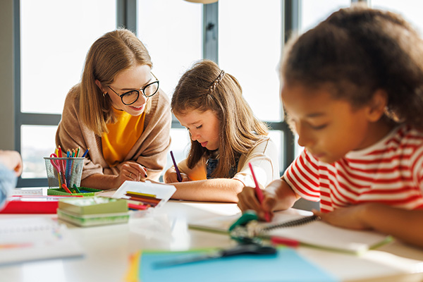 Junge Lehrerin unterstützt Schülerinnen beim Schreiben, Foto: Evgeny Atamanenko/Shutterstock