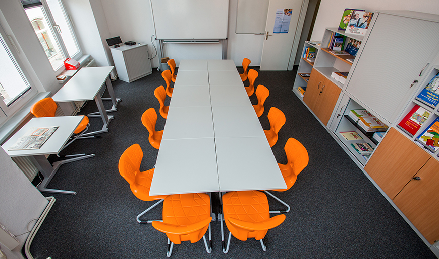 Ein menschenleerer Tagungsraum mit orangenen Stühlen, die um einen Tisch stehen.