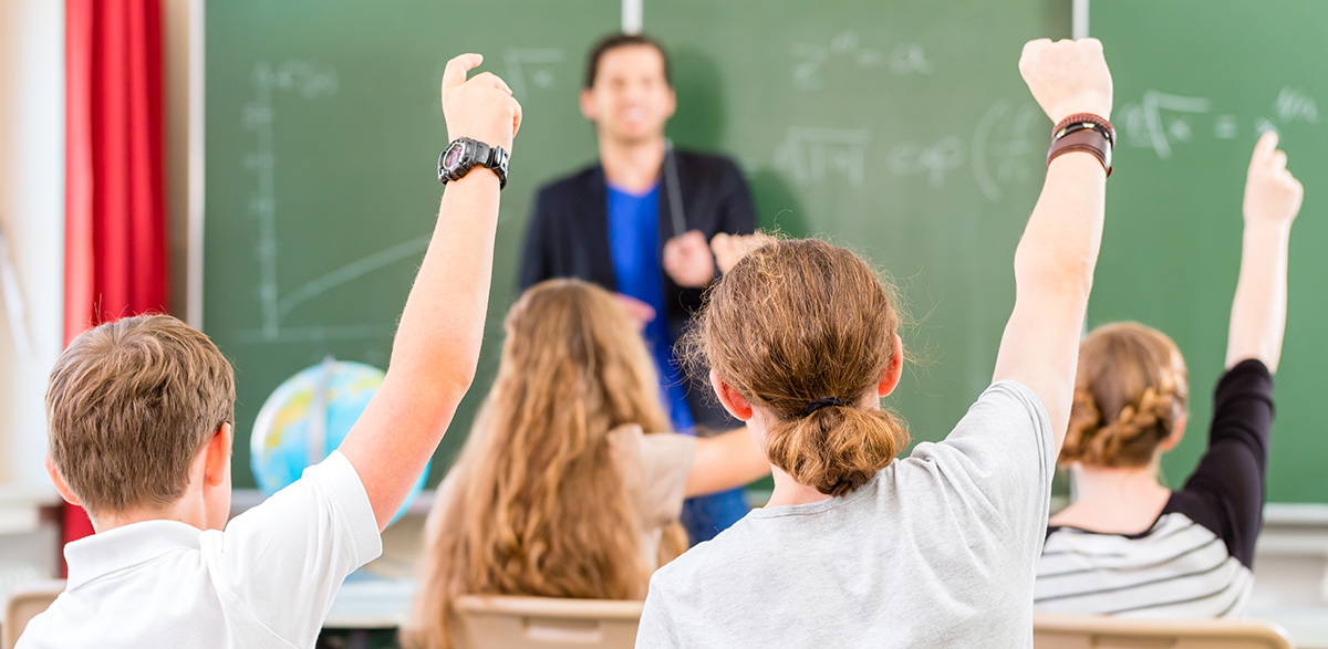 Ein Lehrer steht vor Tafel und spricht mit den Schülern, Foto: colourbox