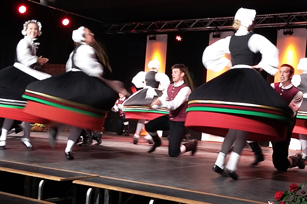 Frauen und Männer tanzen in Trachten auf einer Bühne beim Folklorefestival in Ribnitz-Damgarten.