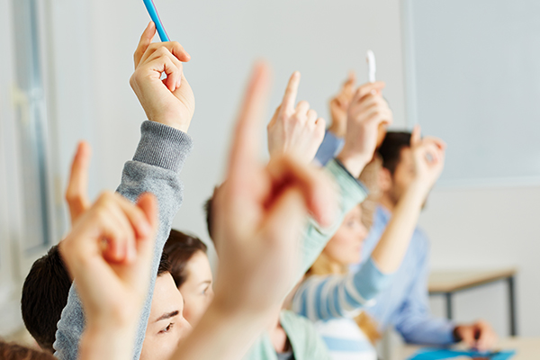 Viele Schüler heben im Unterricht ihre Hände. Foto: Fotolia/Robert Kneschke