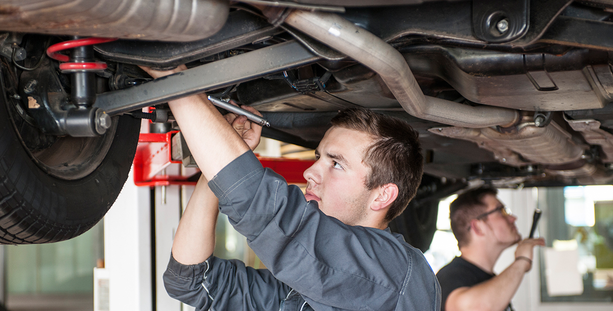 Zwei angehende Kfz-Mechatroniker prüfen den Unterboden eines Autos, das auf einer Hebebühne steht. Foto: Jörn Lehman, © Handwerkskammer Schwerin