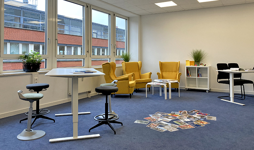 Blick in einen Beratungsraum mit Sitzecke mit Sesseln und kleinen Tischen sowie höhenverstellbarem Beratungstisch mit Hockern, Foto: KBS