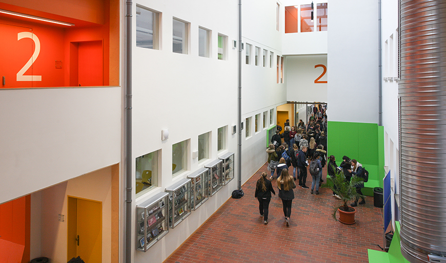 Eine der energietechnisch modernsten Schulen in Deutschland: das Gymnasium Reutershagen nach Fertigstellung des Projekts „Plus-Energie-Schule“ 2015 – mit farbenfrohem Innenleben und Windrädern sowie Sonnenkollektoren auf dem Schulgelände.