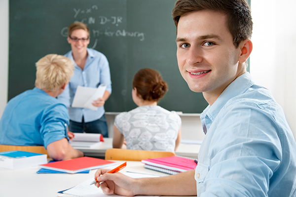 Junger Mann im Klassenzimmer dreht sich um und schaut in die Kamera, Foto: Alexander Raths/shutterstock.com