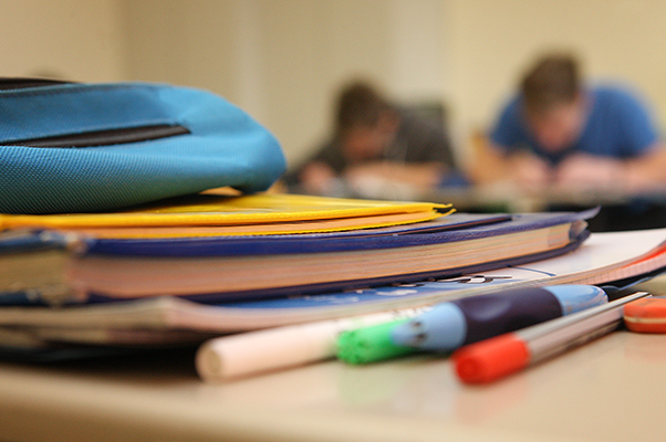 Im Vordergrund liegen Hefte und Stifte auf dem Tisch, im Hintergrund sitzen Schüler am Tisch, Foto: Silke Winkler