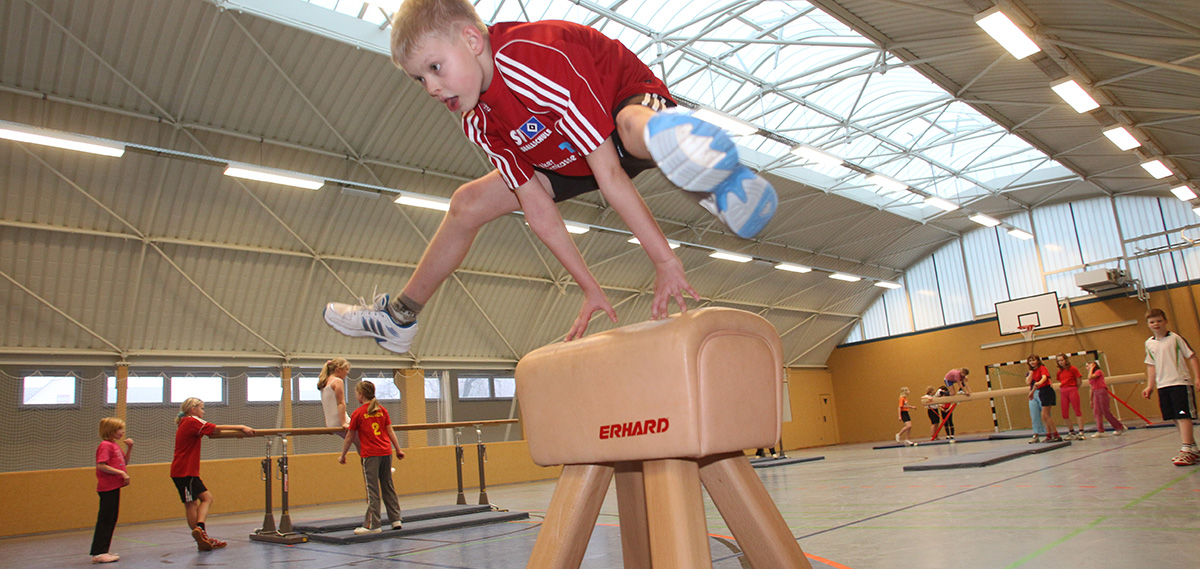 In einer Sporthalle springt ein Junge über einen Bock und andere Schülerinnen und Schüler turnen am Barren, Foto: Danny Gohlke