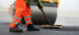 Straßenwalze und Bauarbeiter mit Besen bei der Asphaltfertigung