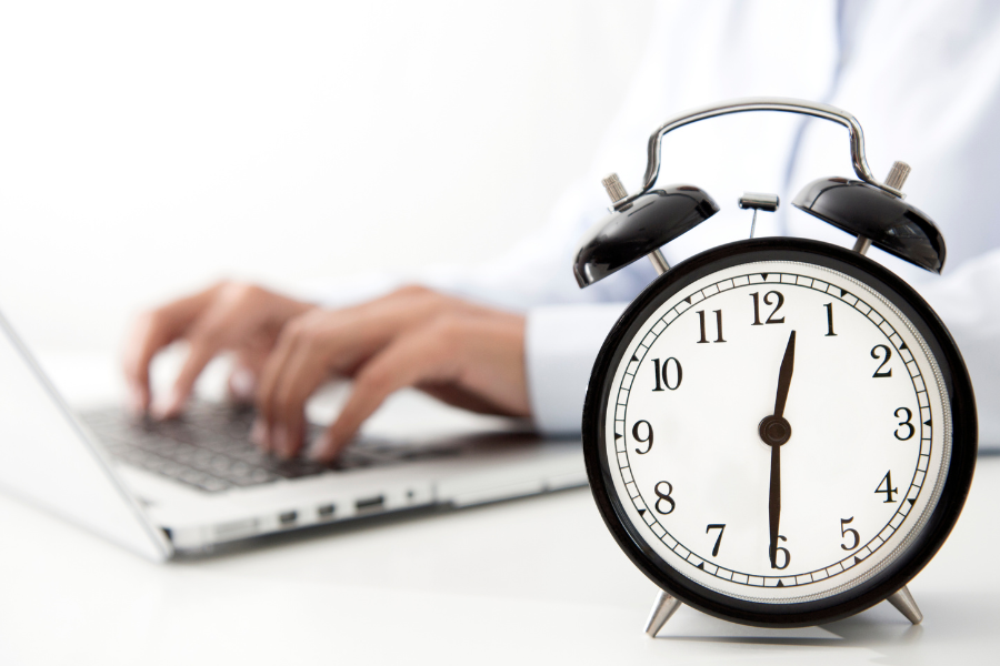 Im Hintergrund Hände, die auf Laptop tippen, im Vordergrund eine Uhr © Getty Images/Canva