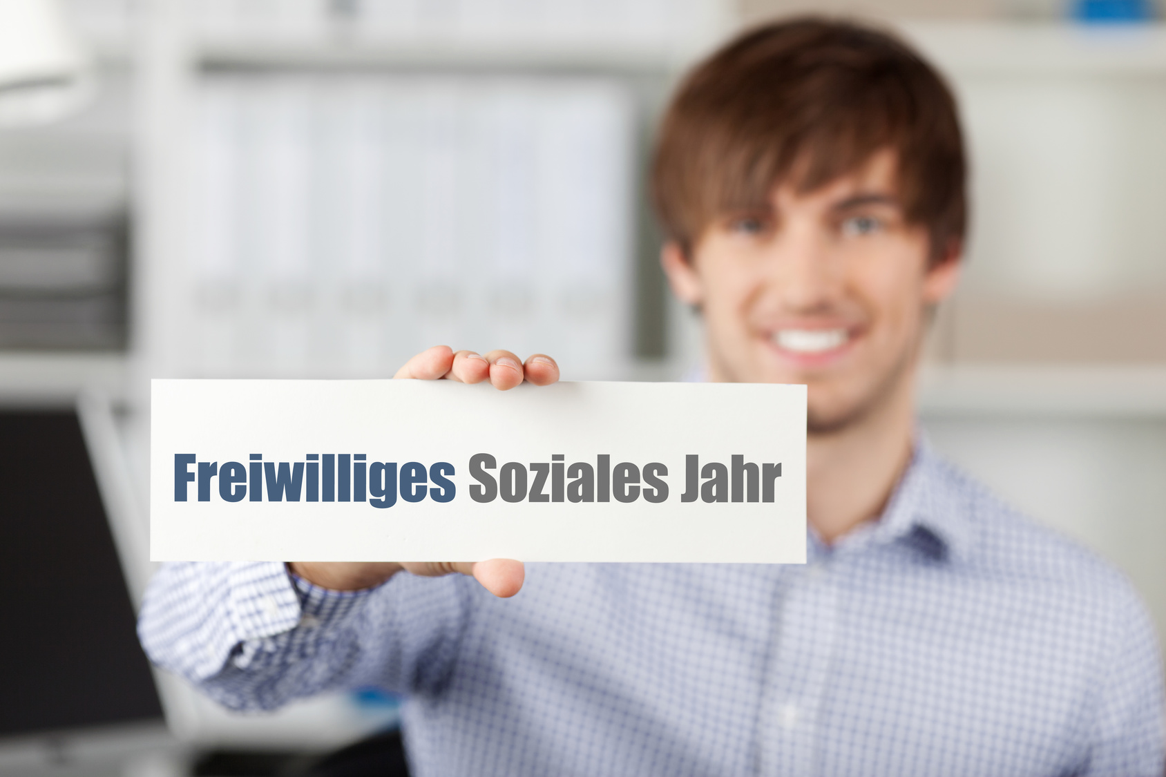 Foto von einem jungen Mann, der ein Schild in die Kamera hält. Darauf steht "Freiwilliges Soziales Jahr"