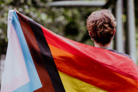 Symbolbild: Mensch ist von hinten zu sehen und hält Regenbogenflagge