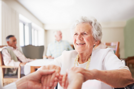 Ältere Frau reicht einer Person außerhalb der Bildausschnittes lachend die Hände