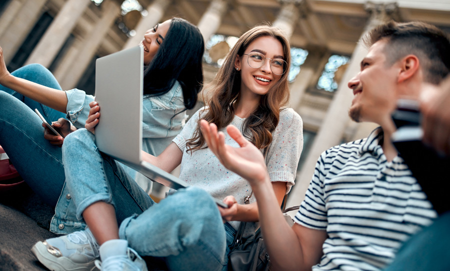 Studenten mit Laptops sitzen auf einer Treppe vor dem Universitätsgebäude