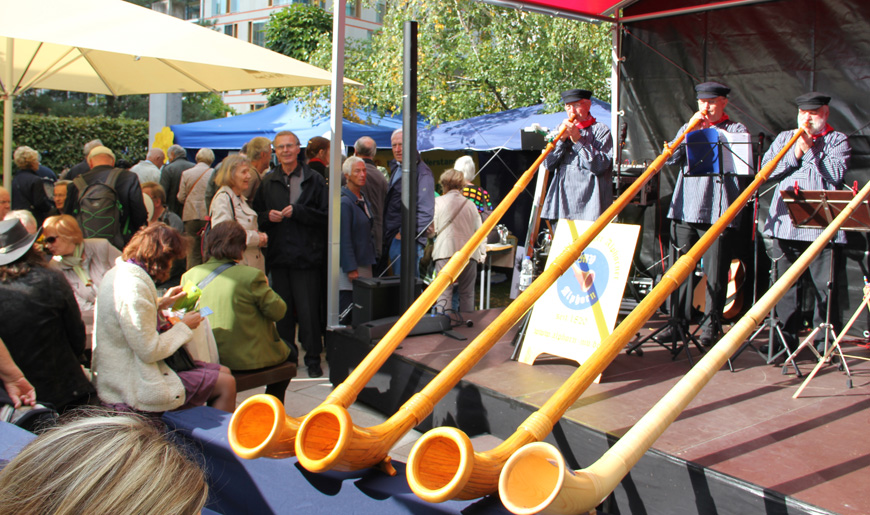 Vier Alphörner werden von Männern auf einer Bühne geblasen