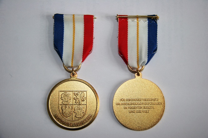 Runde Medaille mit Landeswappen auf der einen Seite und Ordenstext "Für besondere Verdienste um Mecklenburg-Vorpommern im vereinten Europa und der Welt" auf der anderen Seite