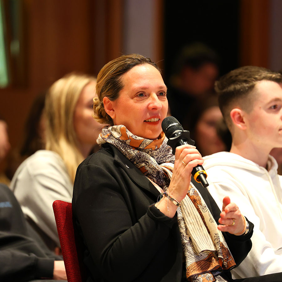 Am Abend begrüßt die Bevollmächtigte des Landes, Staatssekretärin Jutta Bieringer, die Gäste in der Landesvertretung. Sie sitzt in einer Stuhlreihe und hält ein Mikrophon in der Hand.