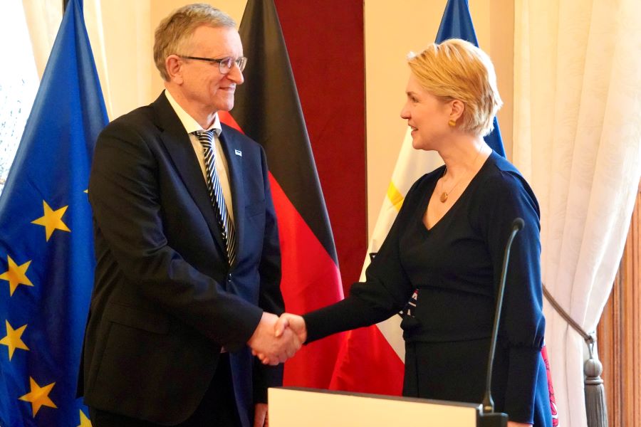 Schwesig mit Dr. Friedrich-Wilhelm Hagemeyer, dem sie zu seiner Auszeichnung gratuliert. Im Hintergrund sind die EU- sowie die Deutschland- und MV-Flagge zu erkennen.