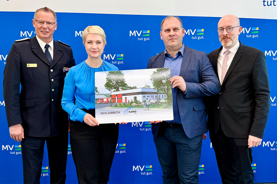 Landesbrandmeister Hannes Möller, Ministerpräsidentin Manuela Schwesig, Wotan Drescher, Geschäftsführer von KAWO Ing sowie der Minister für Inneres und Bau Christian Pegel. Schwesig und Drescher halten eine Abbildung des Musterfeuerwehrhauses hoch.