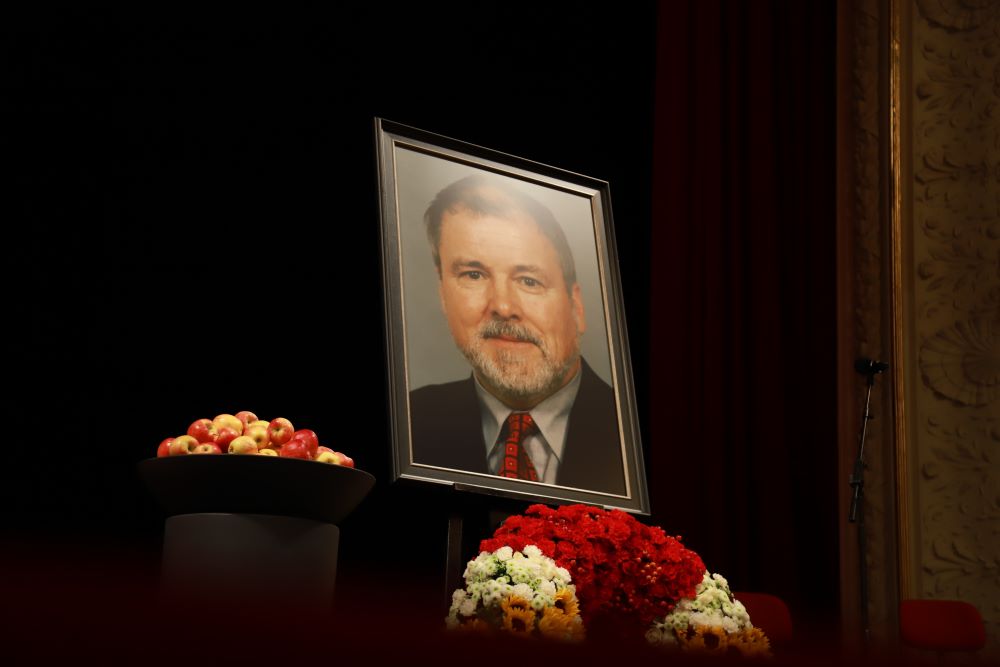 Das Bild zeigt ein großes aufgestelltes Portrait von Harald Ringstoff. Darunter befindet sich ein Blumenkranz und daneben eine Schale voller Äpfel.