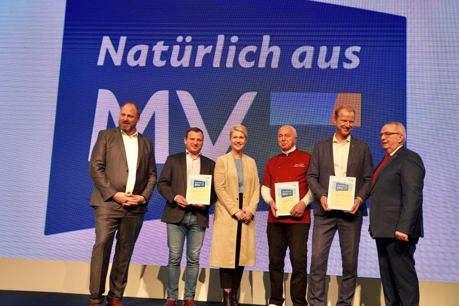 Gruppenbild, mit dem neuen Regionalzeichen "Natürlich aus MV" im Hintergrund, mit Ministerpräsidentin Manuela Schwesig, Minister Dr. Till Backhaus, dem Vorsitzendes der AMV-Marketinggesellschaft Tobias Blömer sowie, ihre Urkunden haltend, den Geschäftsführern Armin Kremer (Mecklenburger Landpute), Ulrich Deprie (Schokoladerie Juillet de Prie) und Bastian Pochstein (Mecklenburgische Brauerei Lübz).