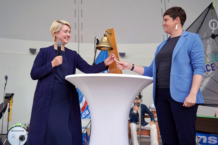 Ministerpräsidentin Manuela Schwesig und Rostocks Oberbürgermeisterin Eva-Maria Kröger beim traditionellen Schlag der Schiffsglocke zur Eröffnung der Hanse Sail. Beide läuten diese gemeinsam an einem Stehtisch.