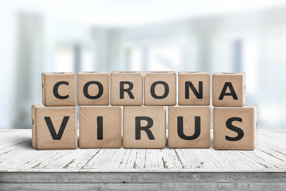 Das Wort "Coronavirus" in jeweils einzelnen Buchstaben auf Holzwürfeln in zwei Reihen auf einen Schreibtisch gelegt