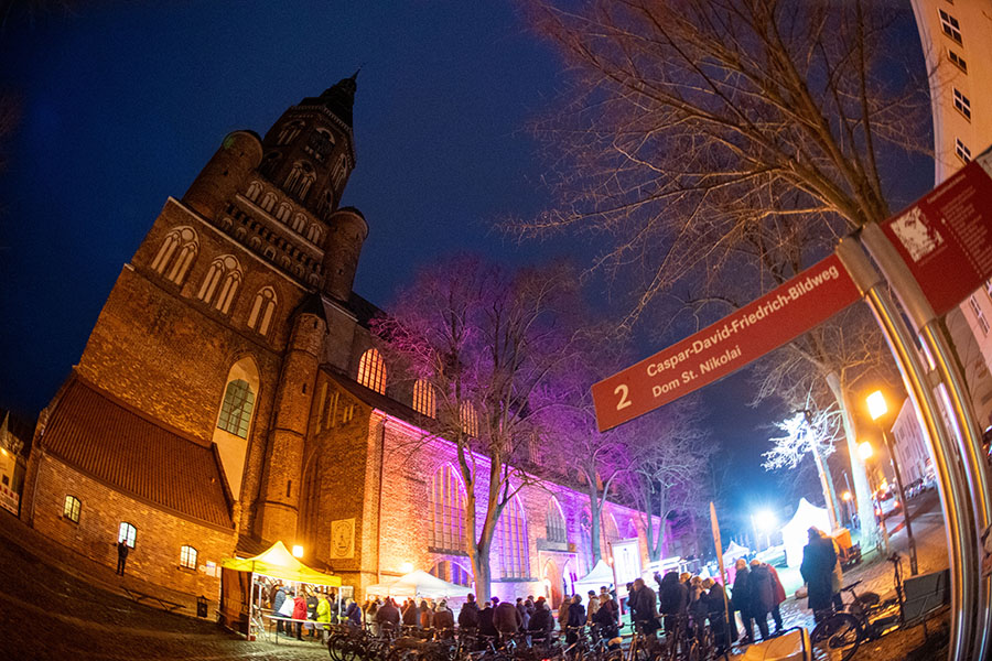 Der festlich in verschiedenen Farben illuminierte Greifswalder Dom St. Nikolai mit wartenden Gästen vor dem Betreten der Veranstaltung