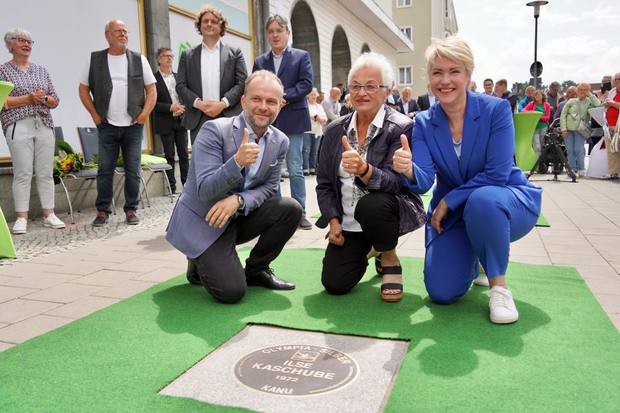 Ilse Kaschube hinter ihrer Bronzeplatte im "Walk of Sport" mit OB Silvio Witt und Ministerpräsidentin Manuela Schwesig. Alle drei strecken einen Daumen in die Höhe.