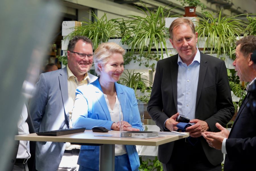 Ministerpräsidentin Manuela Schwesig und der Parlamentarische Staatssekretär Heiko Miraß befinden sich mit einem Vertreter des Vorstands der Firma Durable an einem Stehtisch, einander zugewandt. Im Hintergrund sind im Foyer einige Pflanzen zu erkennen.