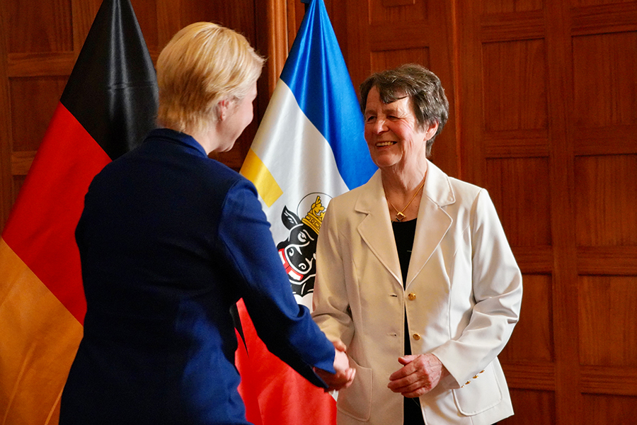 Die Ministerpräsidentin gratuliert Jutta Hastädt zu ihrer Auszeichnung. Im Hingergrund sind die Deutschland- und die Mecklenburg-Vorpommern-Flagge zu sehen.