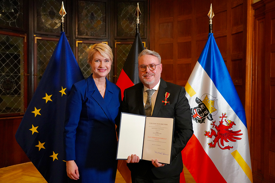 Klaus-Peter Glimm und Ministerpräsidentin Manuela Schwesig halten zusammen die Verleihungsurkunde in die Kamera.