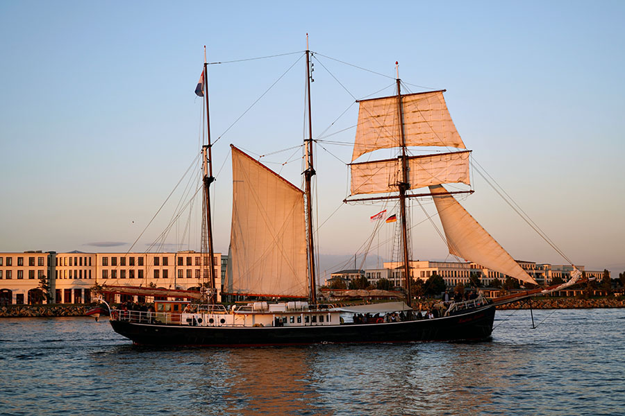 Abendstimmung mit einem Segelschiff, das von der Sonne orangefarben angestrahlt wird