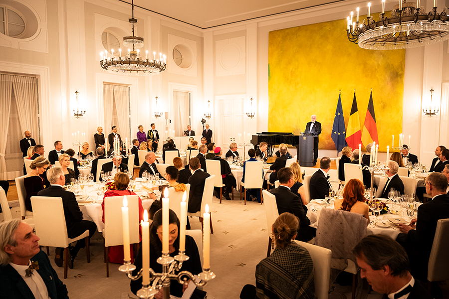 Rede von Bundespräsident Frank-Walter Steinmeier auf dem Staatsbankett auf Schloss Bellevue anlässlich des Staatsbesuchs des belgischen Königspaares. Hinter dem Bundespräsidenten sind die Flaggen der EU, Belgiens und Deutschlands zu sehen. Zu sehen sind einige festlich eingedeckte Tische, an denen die Gäste des Bundespräsidenten sitzen.